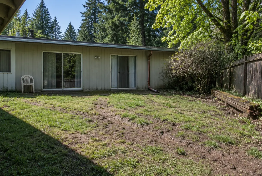 A worn sloping back lawn in Tualatin with bare mud and a rotting sleeper wall